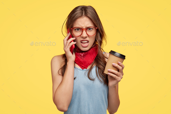 Angry young woman feels intense while has telephone conversation with friend, hears nonsense, disagr