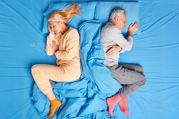Above view of married old couple sleep deeply lying back to each other in comfortable bed wear soft