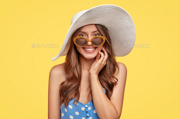 People, beauty and style concept. Content joyful European woman wears white hat, polka dot dress, sh