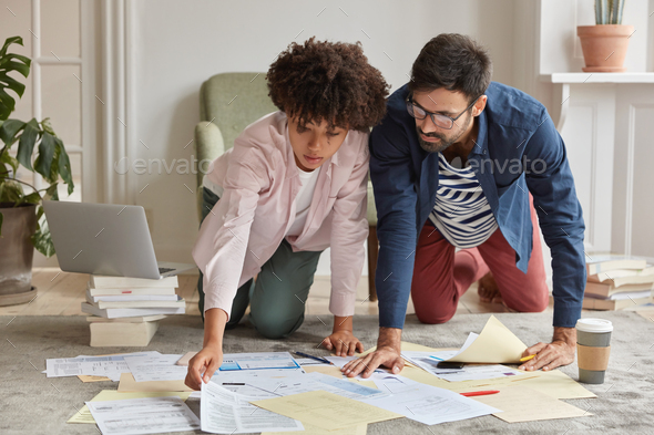 Busy young coworkes stand on knees at floor, focused into documents, prepare financial report for bo - Stock Photo - Images