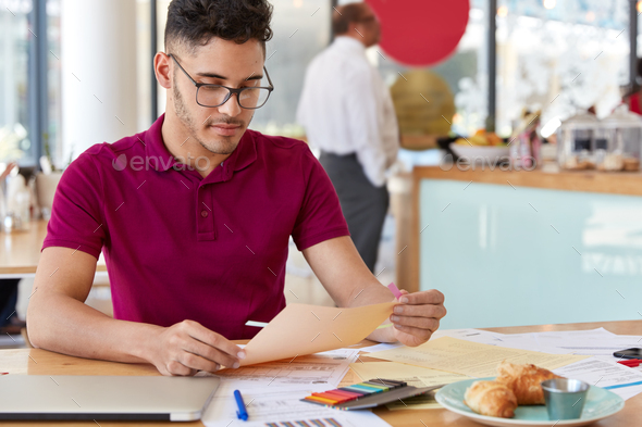Experienced business worker analyzes financial data on papers, being professional economist, dressed