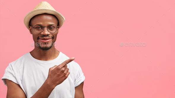 Check this out. Horizontal shot of positive funny African American male in straw hat points with for