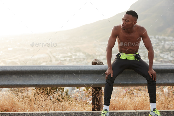 Sporty young man runs with speed, has break after workout in open air near mountains, prepares for s