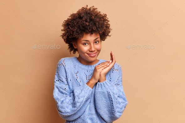 Lovely satisfied woman with Afro hair has satisfied expression rubs palms and smiles gently joyfully