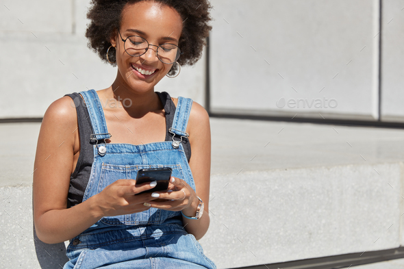 People, recreation and technology concept. Relaxed carefree black woman holds cell phone in hands, t