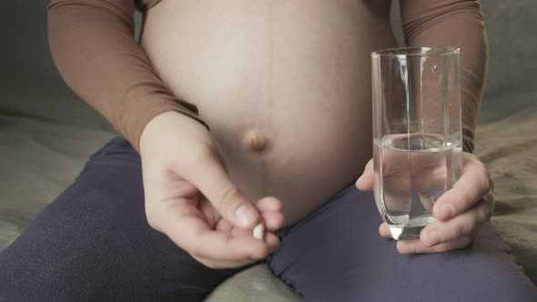 Young Pregnant Woman Sitting on Couch Taking Medicine Drinking Glass of Water