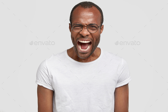 Angry mad African American male exclaims furiously, keeps mouth wide opened, expresses negativity, f