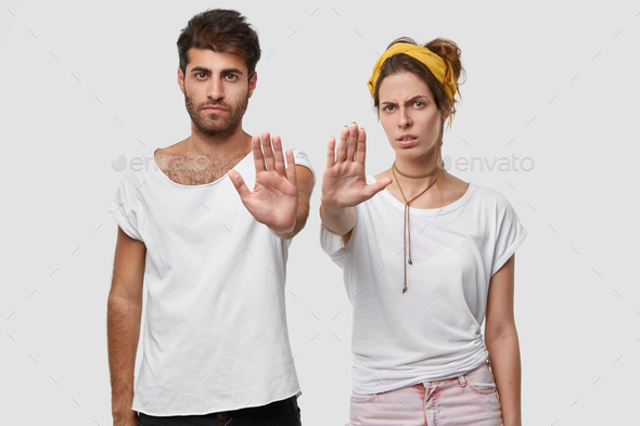 Stay away from us. Displeased young European female and male holds open palm in front of her, demand