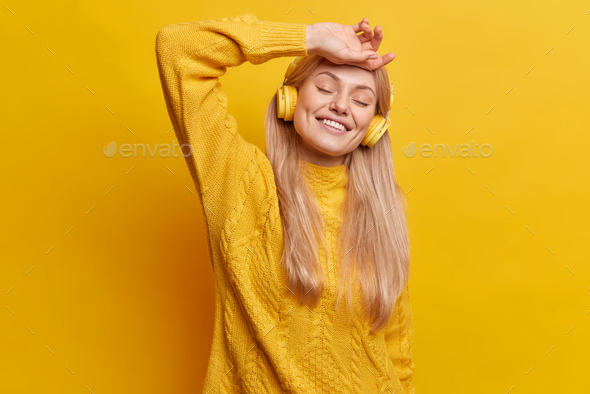 Happy relaxed European woman with long straight hair closes eyes keeps hand on forehead closes eyes