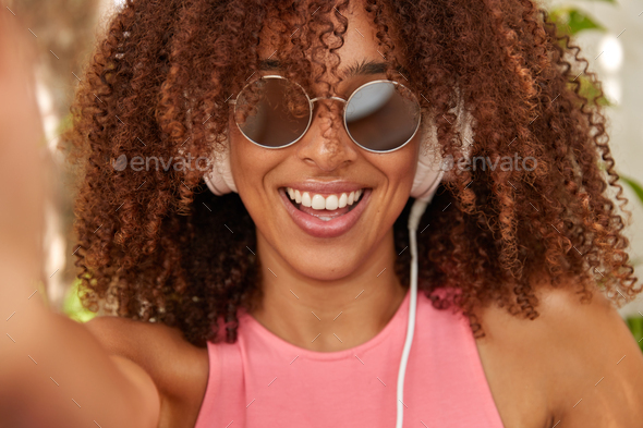 Fashionable black lady with Afro haircut, being real meloman, listens songs from playlist, has trend