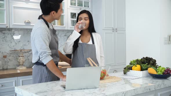 The Young Spouses Use Laptop Computer While Cooking In Kitchen