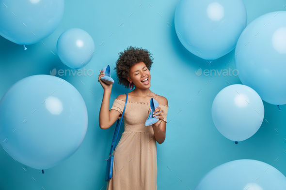 Positive carefree dark skinned woman dressed for birthday party has fun and sings songs wears beige