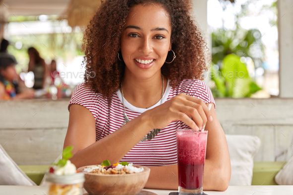 Glad emotive ethnic businesswoman enjoys vacation in foreign country, visit local cafeteria, drinks