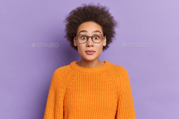 Portrait Of Stunned Curly Millennial Girl Stares Through Spectacles Dressed In Orange Sweater Reacts Stock Photo By Wayhomestudioo