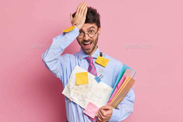 Forgetful student remember about one more task before exam keeps hand on forehead poses with papers