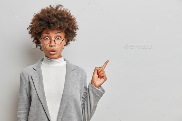 Horizontal shot of shocked ethnic businesswoman has curly bushy hair dressed in grey business clothe