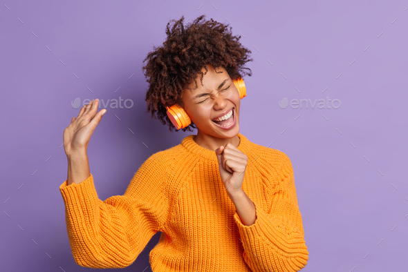Overjoyed carefree young African American woman sings along favorite song feels upbeat wears stereo