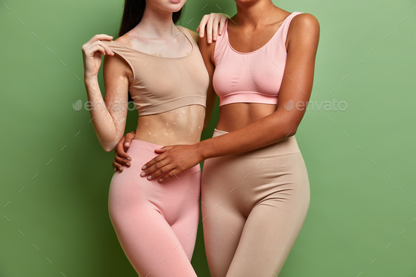 Body shot. Two interracial lesbians with different skins embrace and show flat belly dressed in crop
