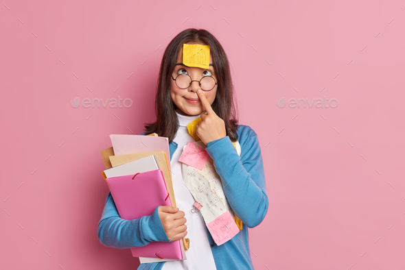 Funny nerdy student touches nose has sticky note with graphic stuck on forehead holds folders and pa