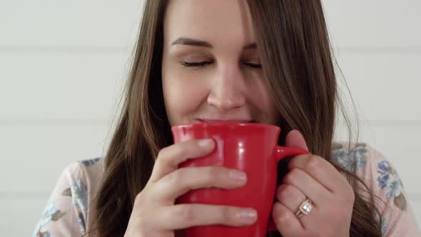 Woman smells hot cup of cocoa and smiles alt