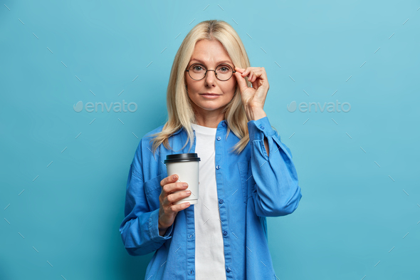 Photo of serious tender adult Caucasian woman looks confidently at camera has coffee break after wor