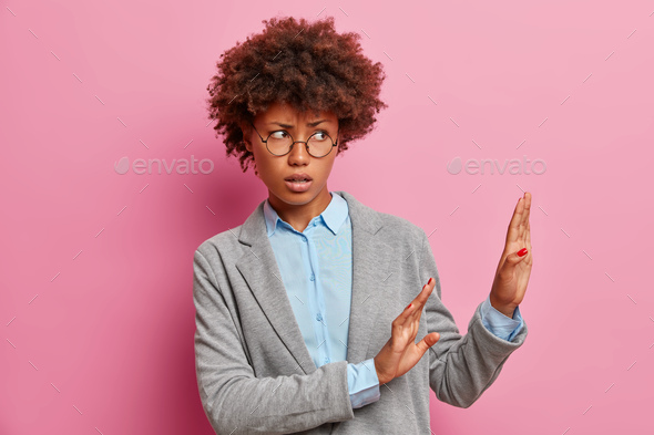 Displeased dark skinned woman keeps palms forward on right side and asks not to come closer refuses