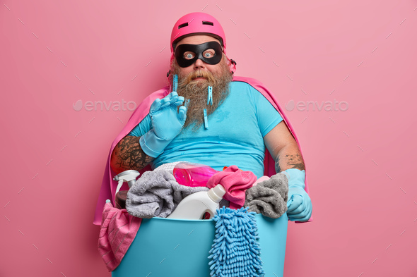 Shocked scared bearded man does laundering at home poses near basin full of dirty towels and deterge