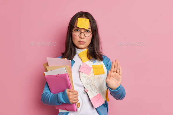 Serious Asian female student does stop gesture keeps palm forward camera asks not to bother her as s