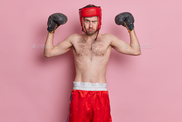 Motivated sportsman enjoys boxing wears protective hat gloves raises arms shows muscles has skinny b