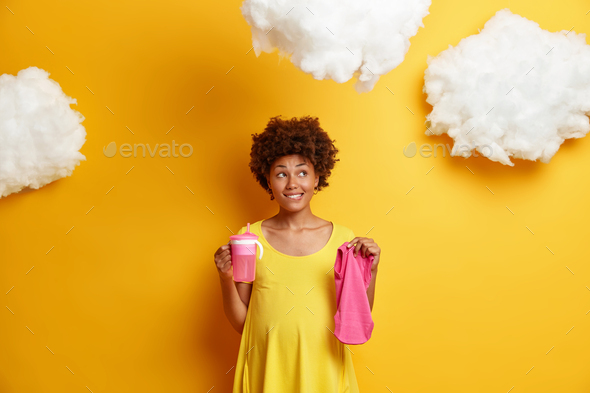 Pensive pregnant young Afro American woman dreams about child and future life holds feeding bottle a - Stock Photo - Images