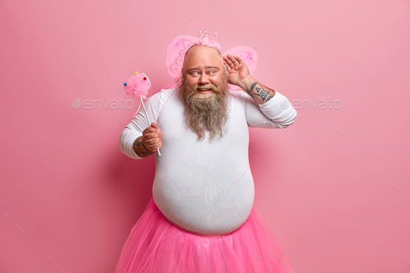 Funny overweight bearded man dressed in fairy costume to entertain guests of party keeps hand near e
