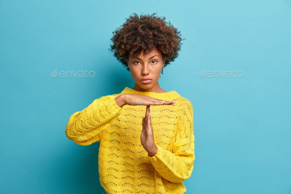 Serious self confident curly haired Afro American woman makes timeout gesture demonstrates limit ask