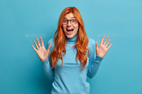 Happy carefree emotions. Excited redhead woman raises palms and looks gladfully at camera screams wi