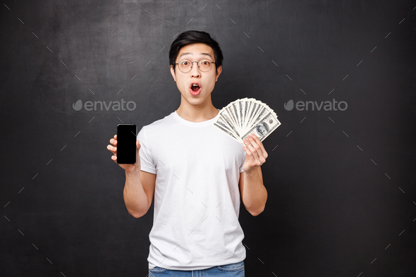 Technology, money and prizes concept. Amazed and surprised asian guy holding dollars, big cash and