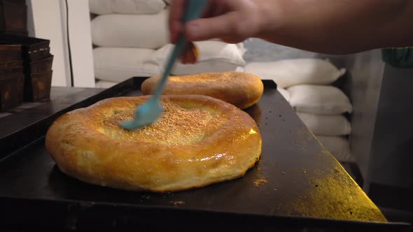 a cook combing melting butter with brush on baked bread alt