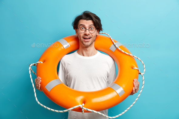 Positive surprised man poses with inflated lifebuoy wears round spectacles and white t shirt eager t - Stock Photo - Images