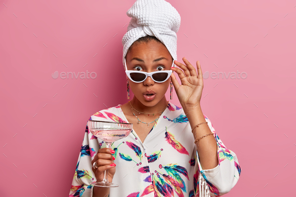 Surprised Dark Skinned Lovely Woman Keeps Hand On Sunglasses Looks With Shocked Expression At