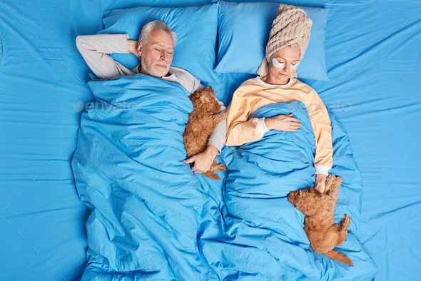 People wellness napping concept. Mature woman and man sleep well in comfortable bed their puppies po