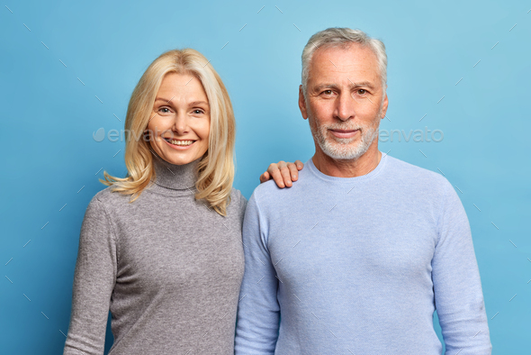 Portrait of mature couple stand next to each other look directly at camera have satisfied expression