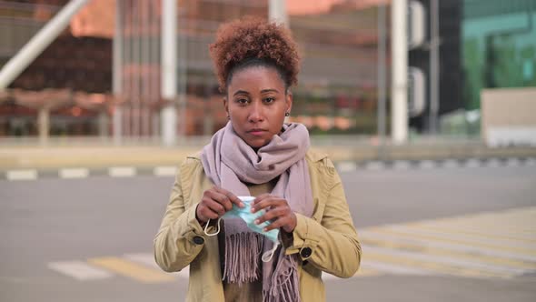Young attractive black woman putting on medical mask against cityscape alt