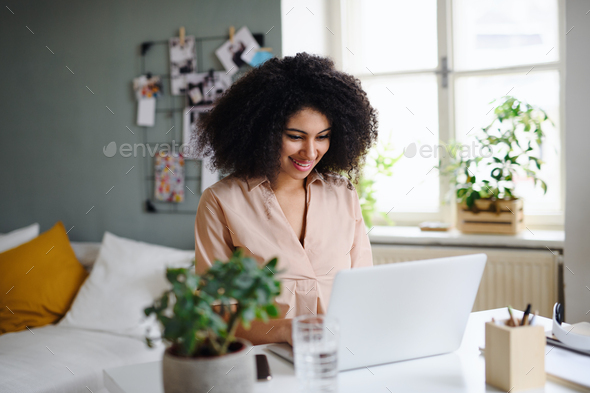 Happy young woman with laptop working indoors at home, home office concept.