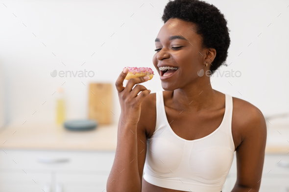 Black Woman Having Cheat Meal Eating Sweet Donut In Kitchen