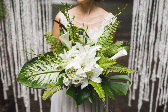 Bride holding in hands huge green bouquet with tropical leaves and flowers
