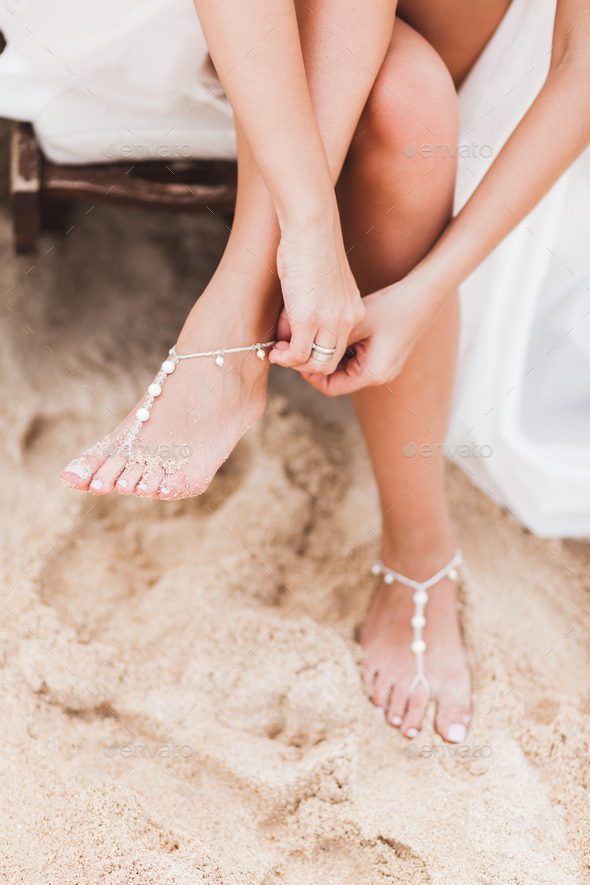 Woman wearing adornment on feet, standing on sandy beach, wedding day, brides style