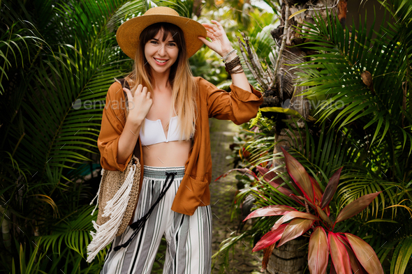 Well-dressed woman in perfect mood playfully posing in tropical garden.