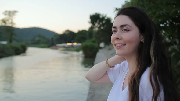 Portrait of a young beautiful woman looking at the river, turning and smiling sweetly alt