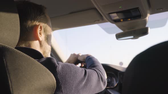 A Middleaged Handsome Caucasian Man Drives a Car on a Road  Rear Low Closeup From the Backseat