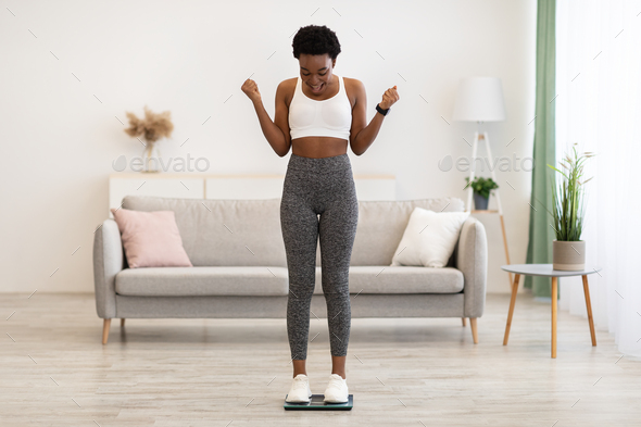 Excited African Woman On Weight-Scales Shaking Fists After Slimming Indoors