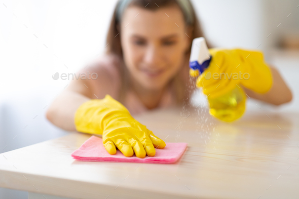 Young housewife in rubber gloves washing table at kitchen with cleanser, selectove focus
