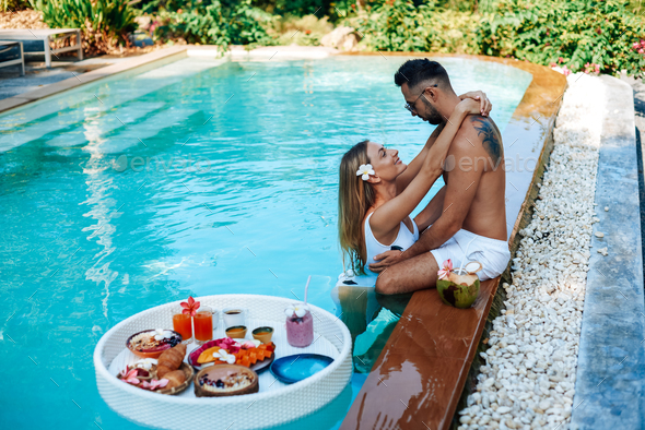 Happy couple of tourists swim in pool and enjoy asian food